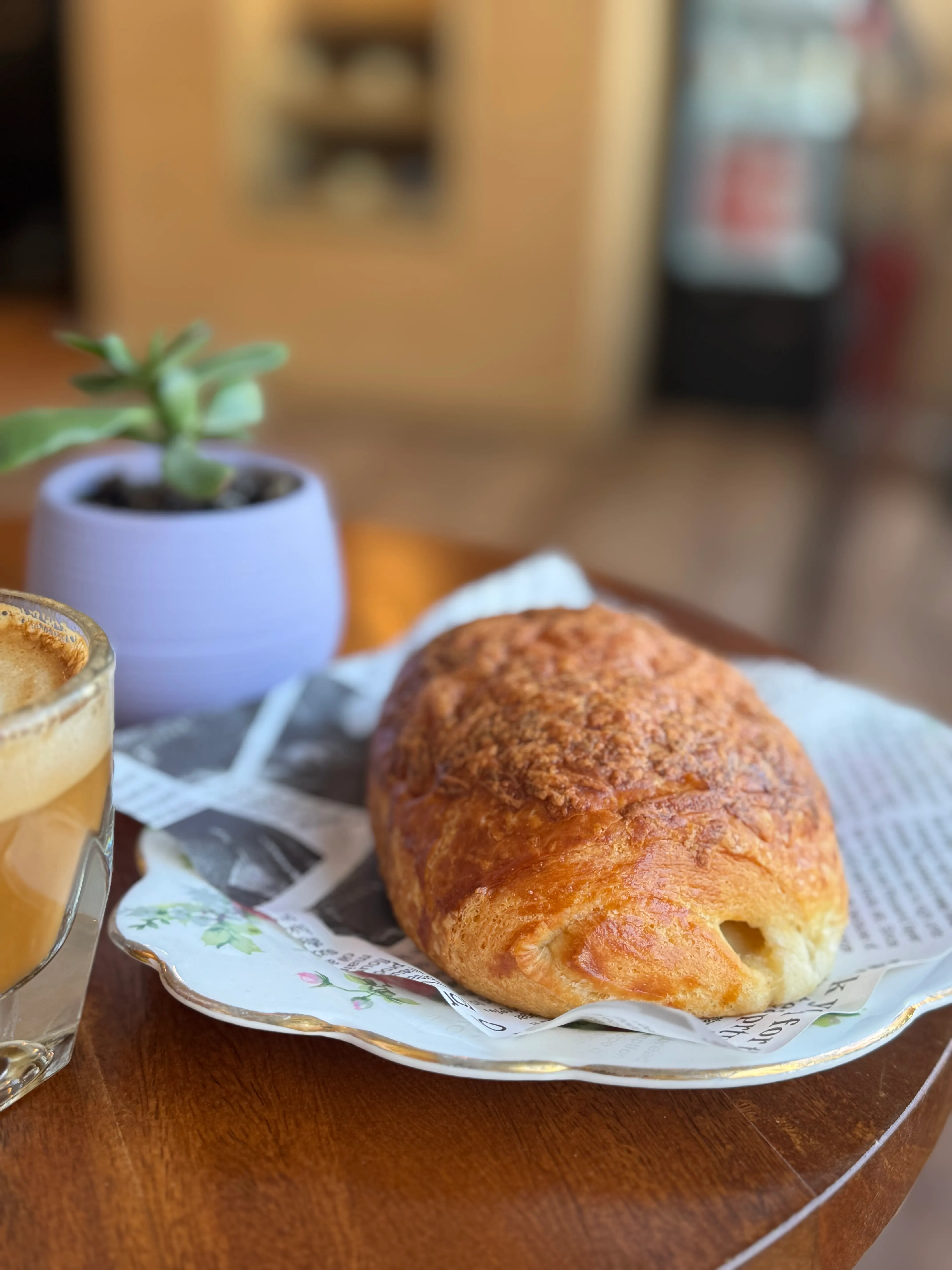 Ham and cheese croissant served on a floral plate beside coffee